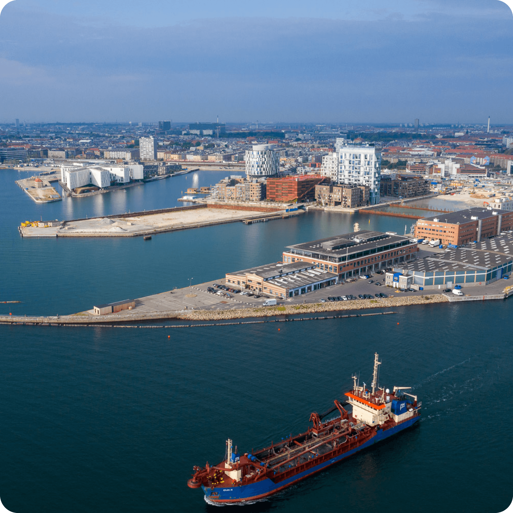 Aerial view of Copenhagen harbour showing a cargo vessel on the water and the city waterfront, representing Copenhagen Merchants Group the family-owned parent company of CM Navigator founded in 1977 with a global network spanning brokerage, trading, shipping and logistics