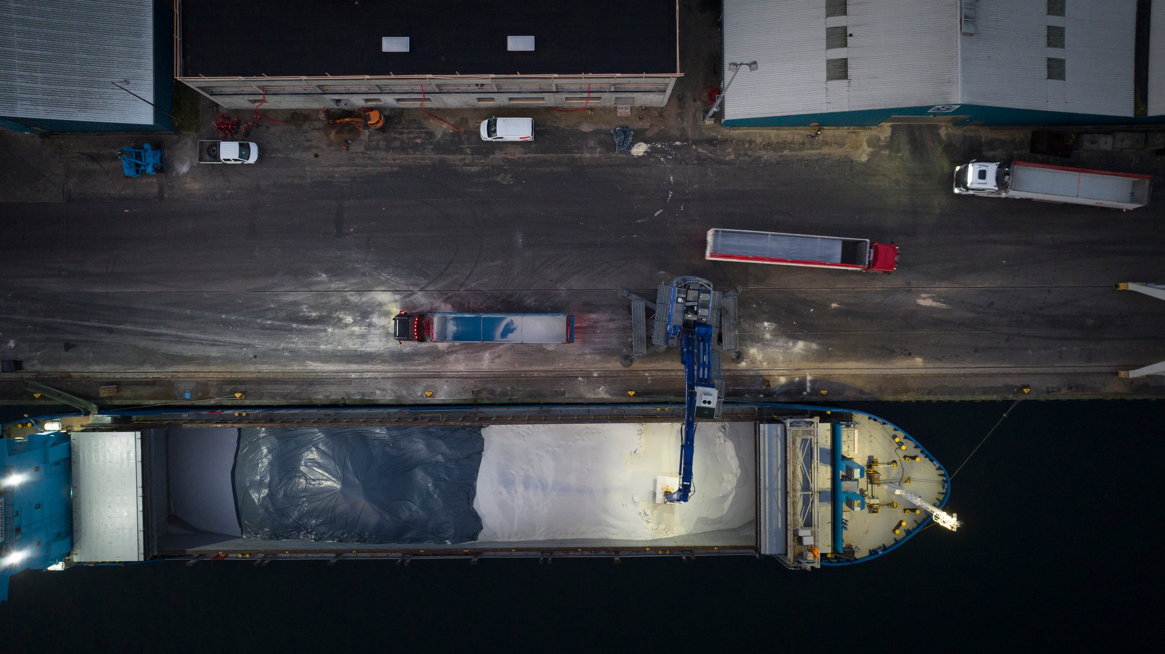 Aerial view of grain being loaded and transported by trucks at a bulk handling facility representing global grain trade flows and the real-time shipment tracking available on the CM Navigator platform